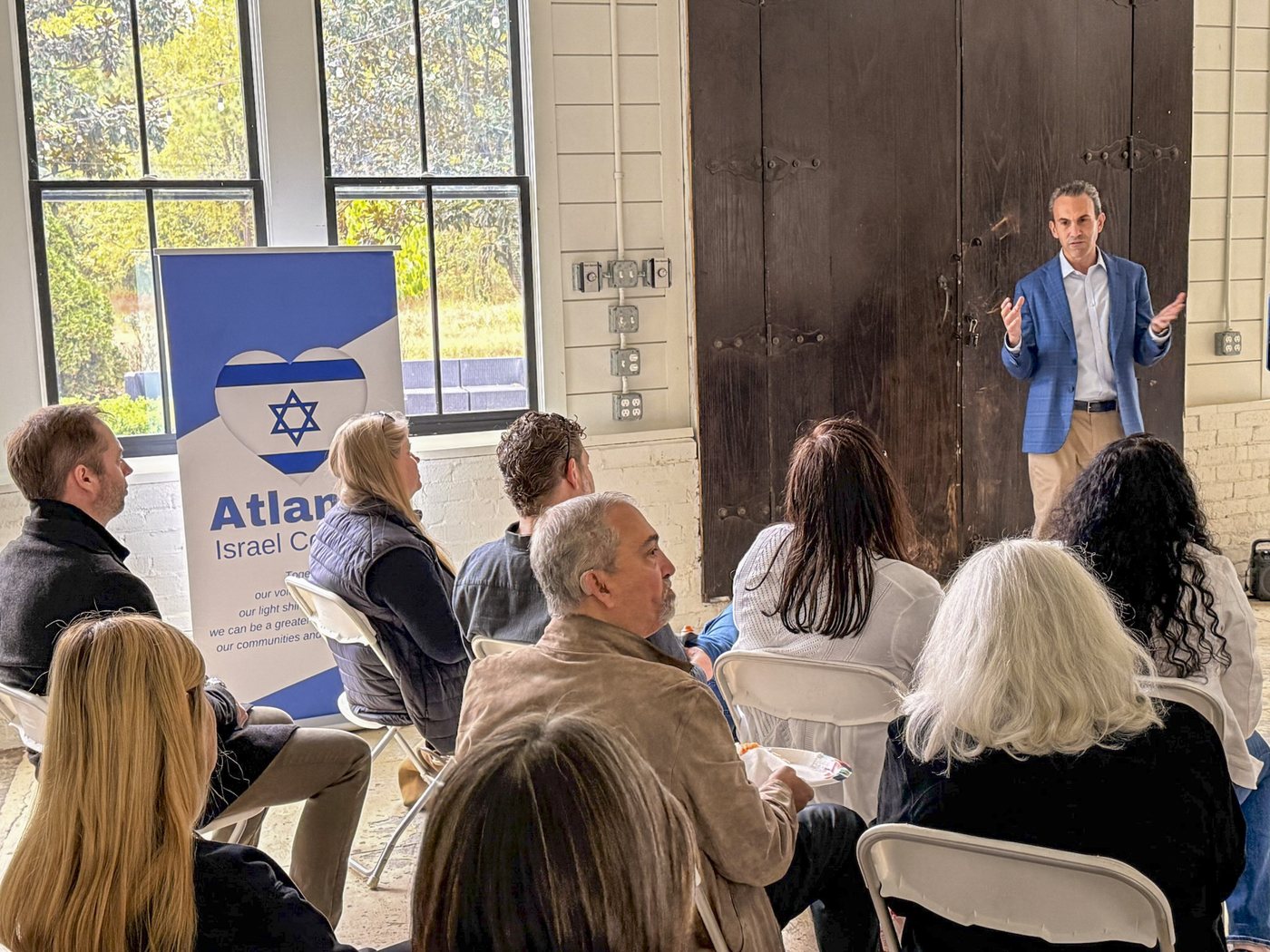 Attendees listen to a speaker at an Atlanta Israel Coalition briefing, the coalition banner beside the stage.