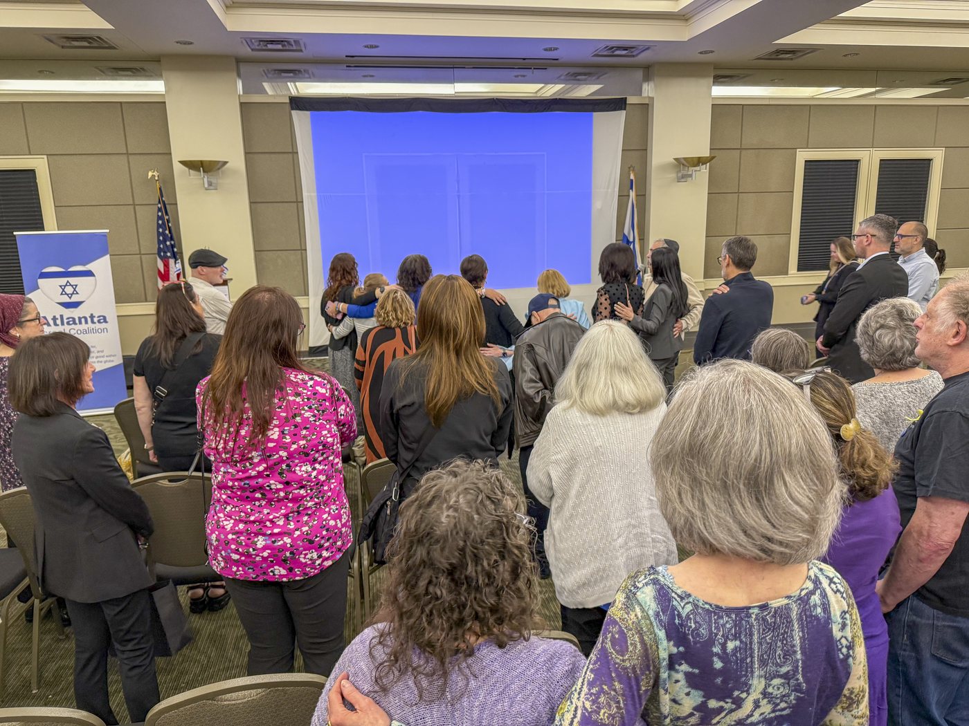 Community members seated at an Atlanta Israel Coalition briefing, the coalition and Israeli flags at the front.