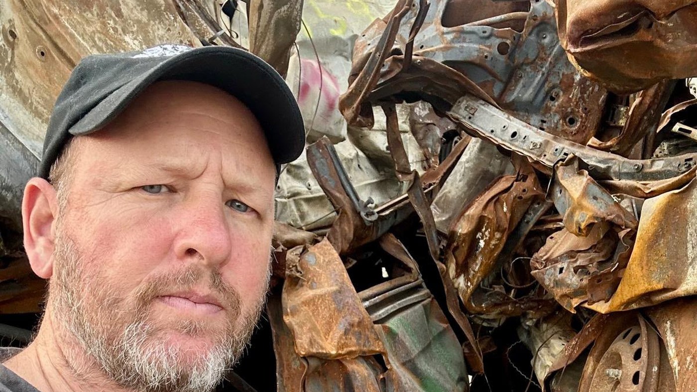 David Sussman standing beside the stacked wreckage of vehicles burned on October 7, collected at the Tkuma site in southern Israel.