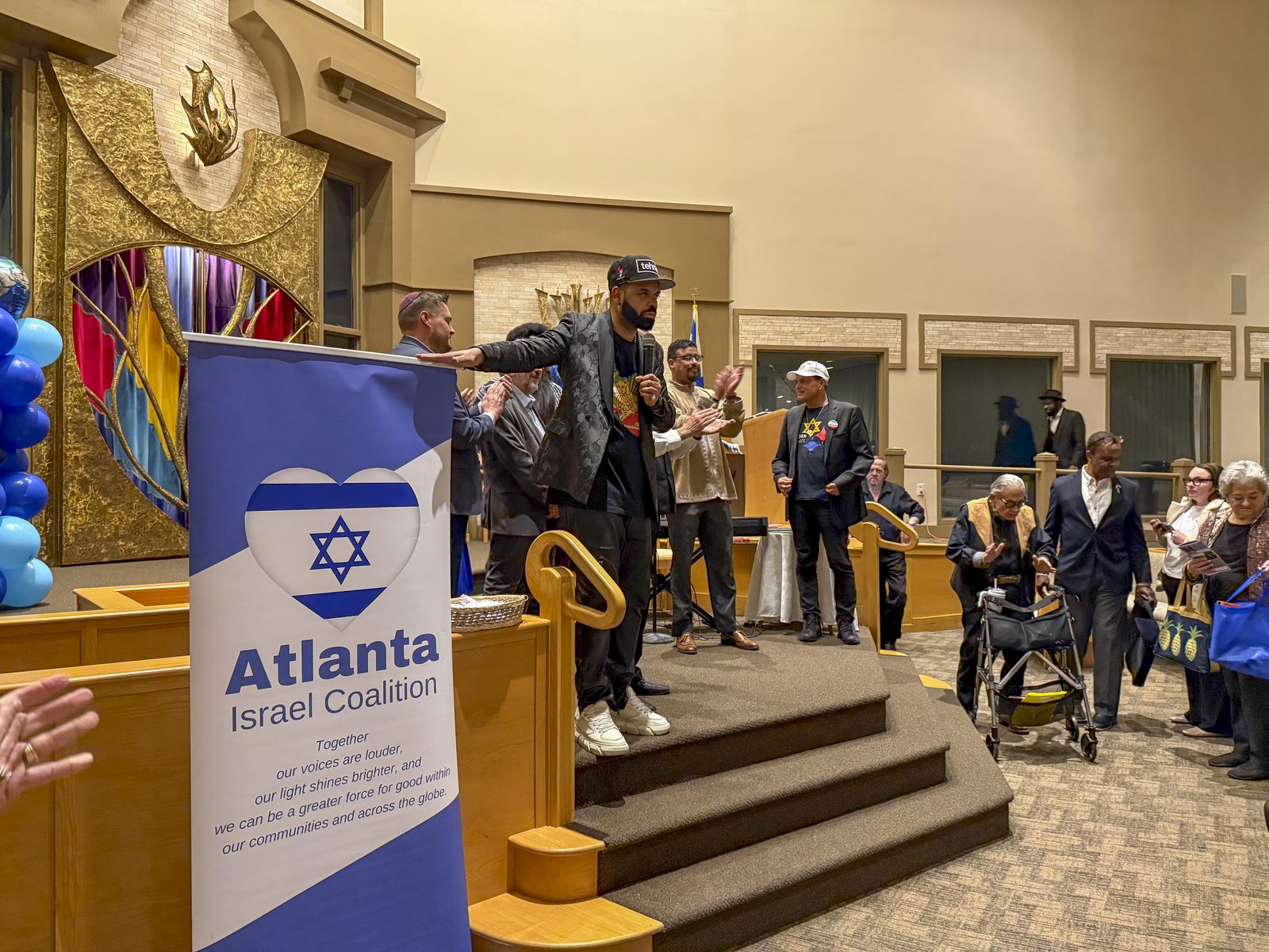 Community members gather beside an Atlanta Israel Coalition podium banner and blue balloons at a coalition celebration.