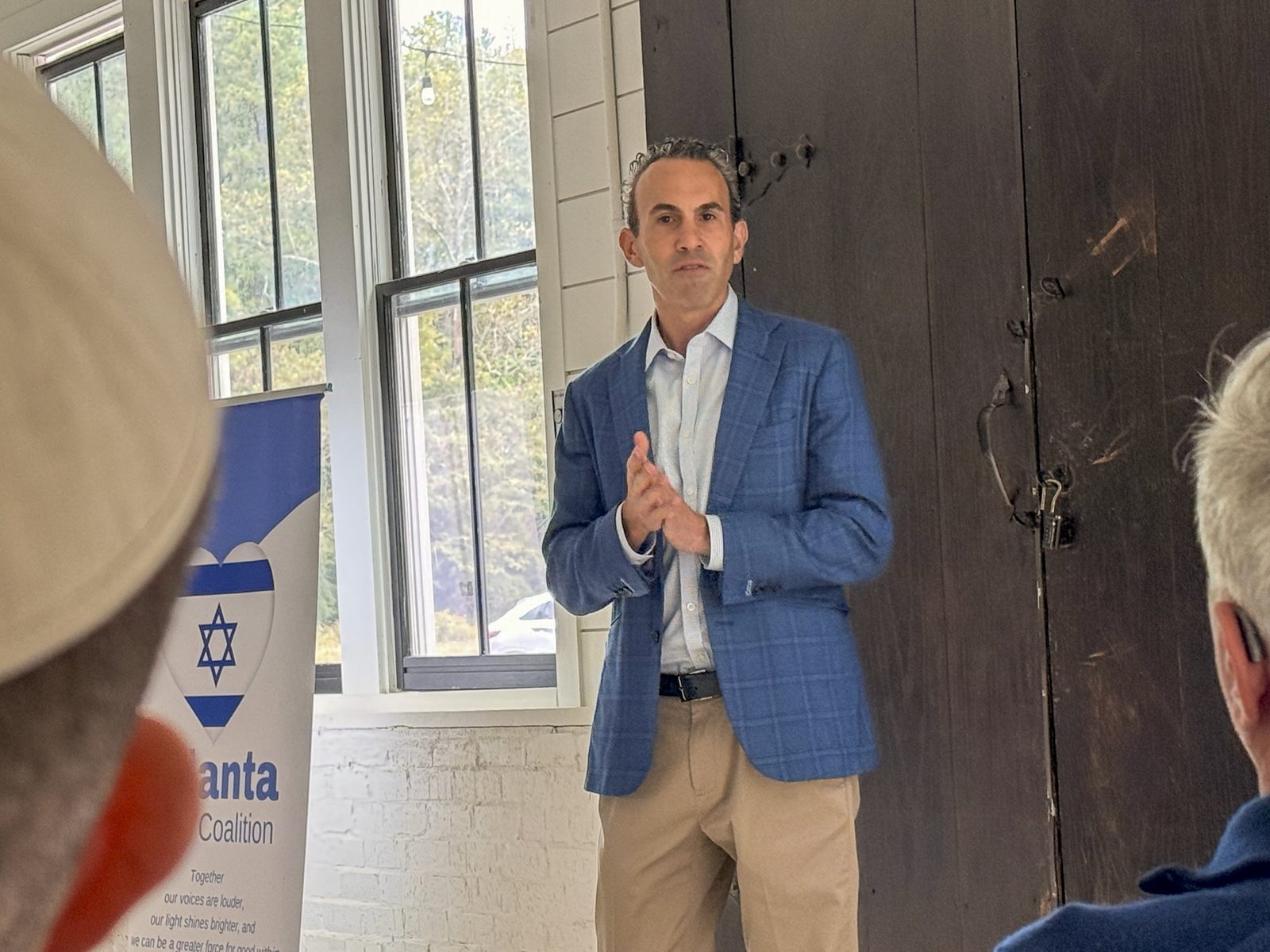 A speaker addresses a seated audience at an Atlanta Israel Coalition briefing, the coalition banner beside him.