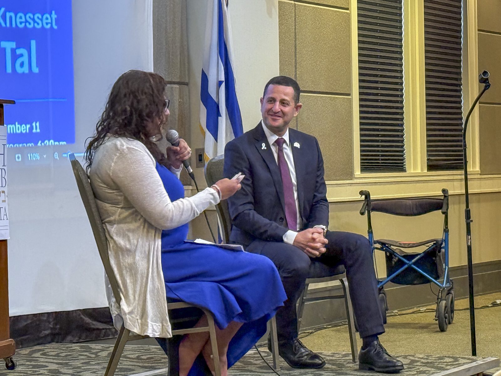 An Atlanta Israel Coalition host interviews a guest on stage beside an Israeli flag during a community event.