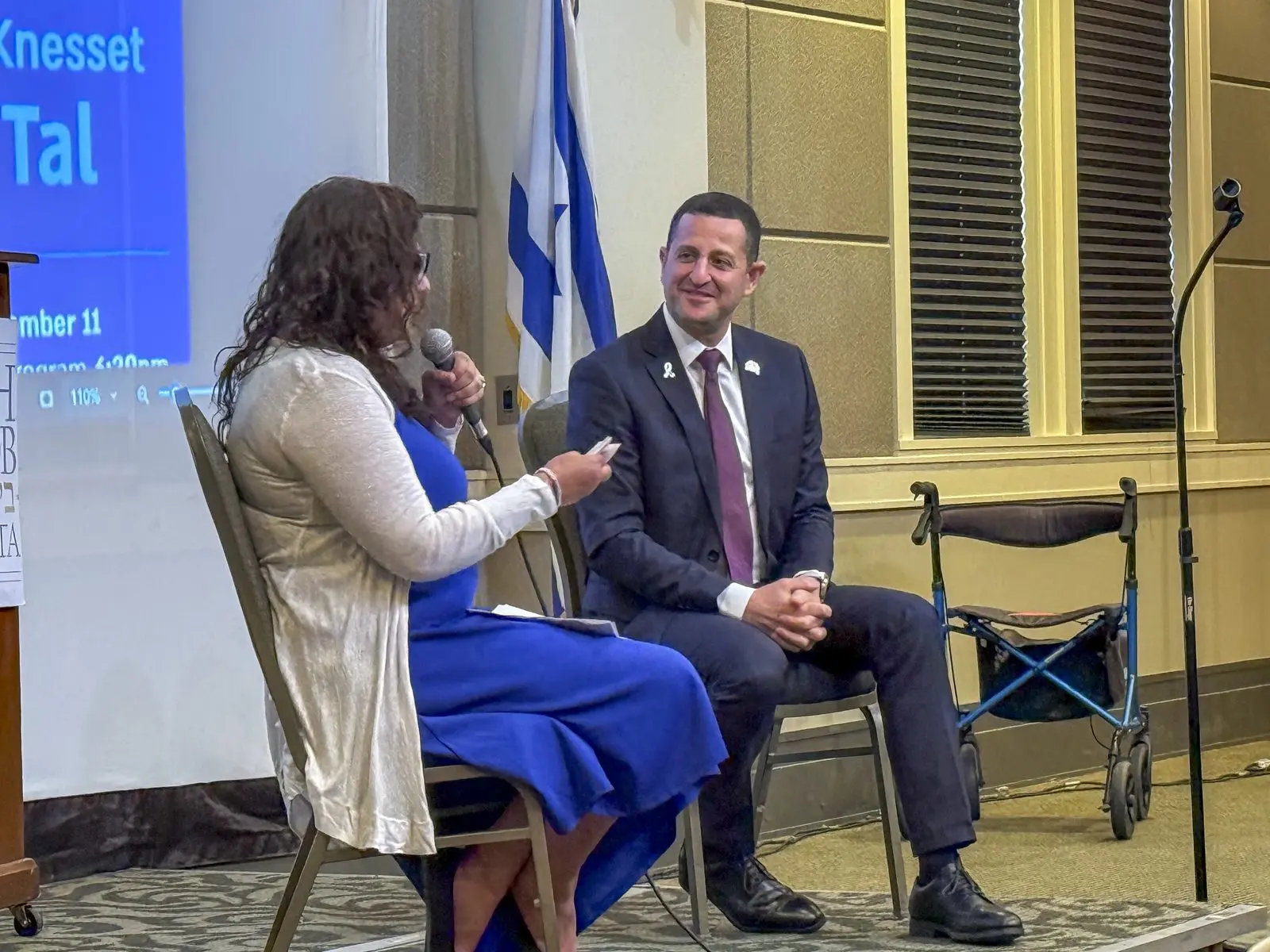 An Atlanta Israel Coalition host interviews a guest on stage beside an Israeli flag during a community event.