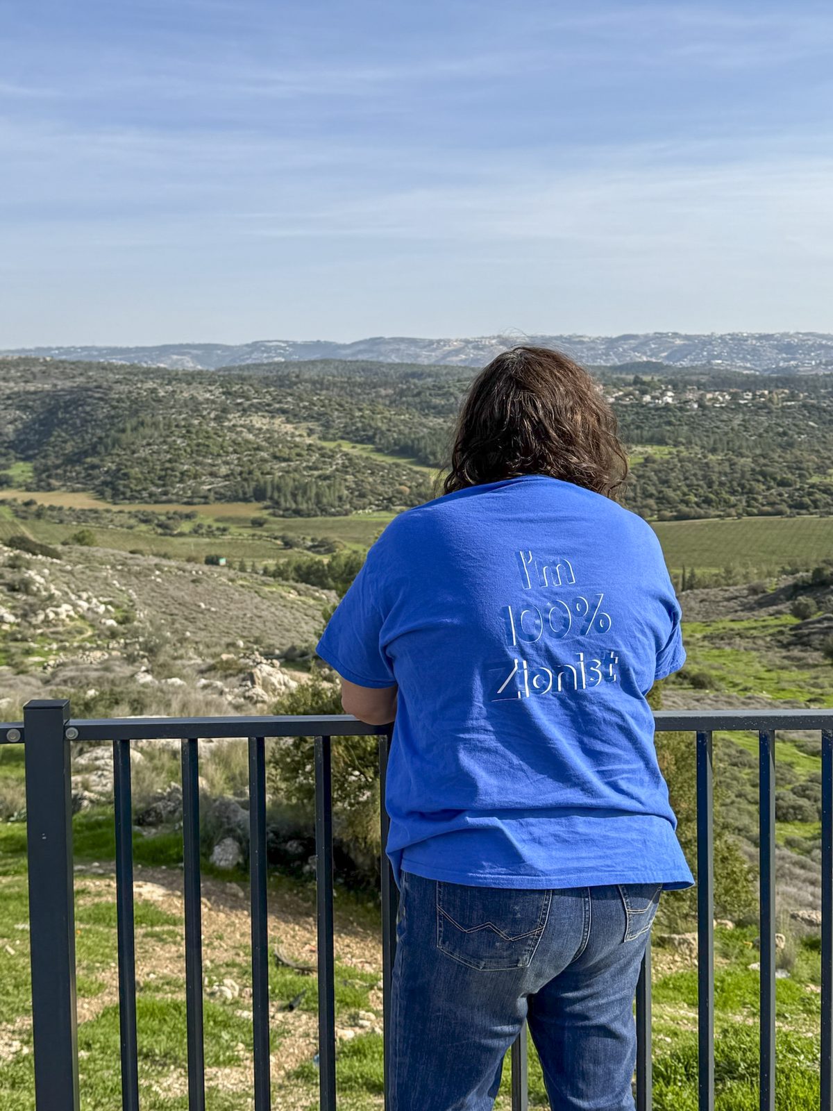 An Atlanta Israel Coalition volunteer in a coalition T-shirt looks out over the green hills of the Galilee.